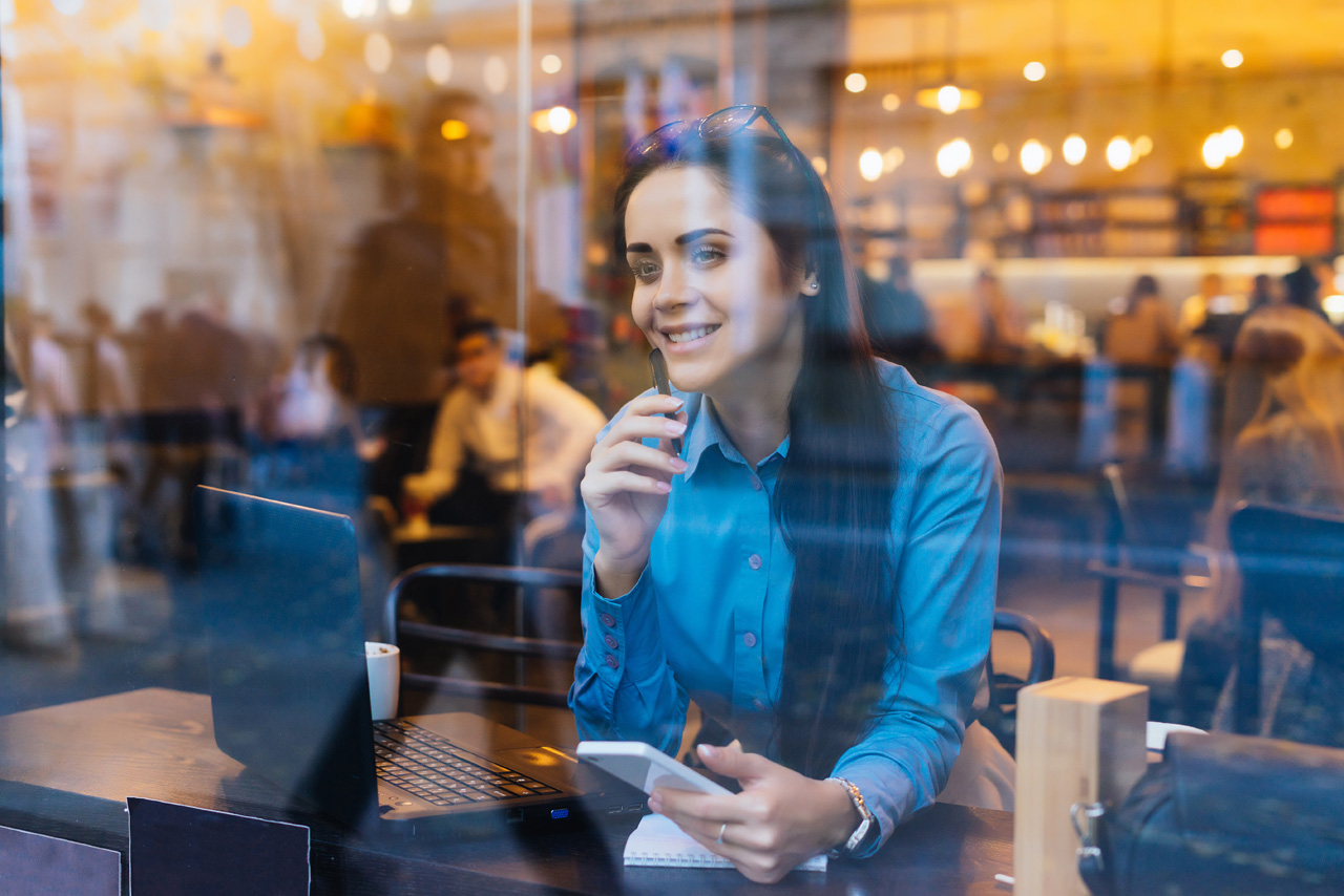 Real estate broker smiling as she works inside of a coffee shop.
